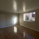 Empty room with wood floor, beige walls, large window, and two white doors