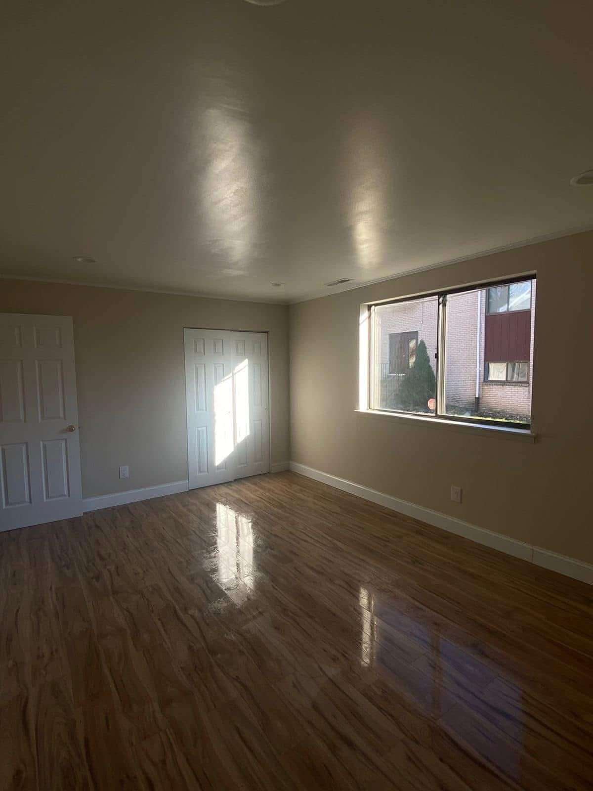Empty room with wood floor, beige walls, large window, and two white doors