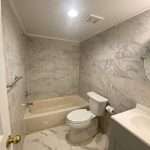 Bathroom with marble tile walls and floor, beige bathtub, toilet, and vanity with sink