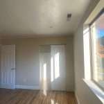 Empty room with wood flooring, large window letting in light, and white door with closet