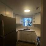 Small kitchen with refrigerator, white cabinets, sink under window, and ceiling light